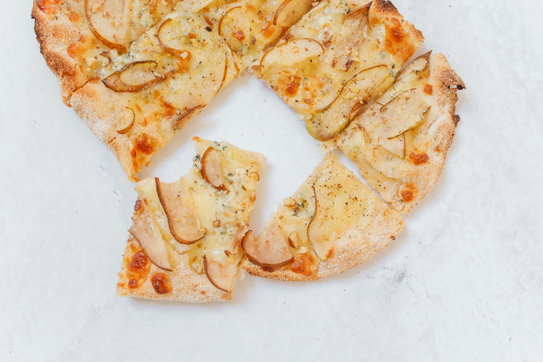 Cienka pizza z gruszką i serem pokrojona na kawałki na białym blacie