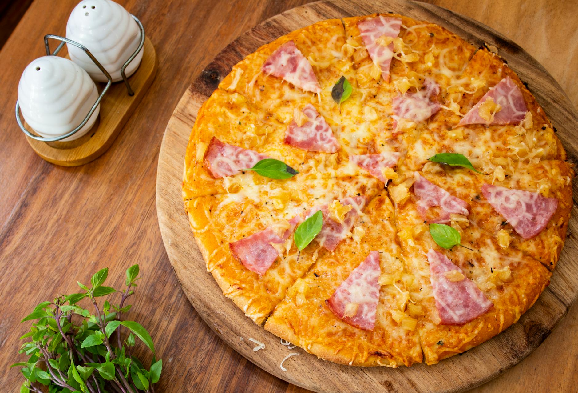 Cienka pizza z szynką, serem i bazylią na drewnianej desce