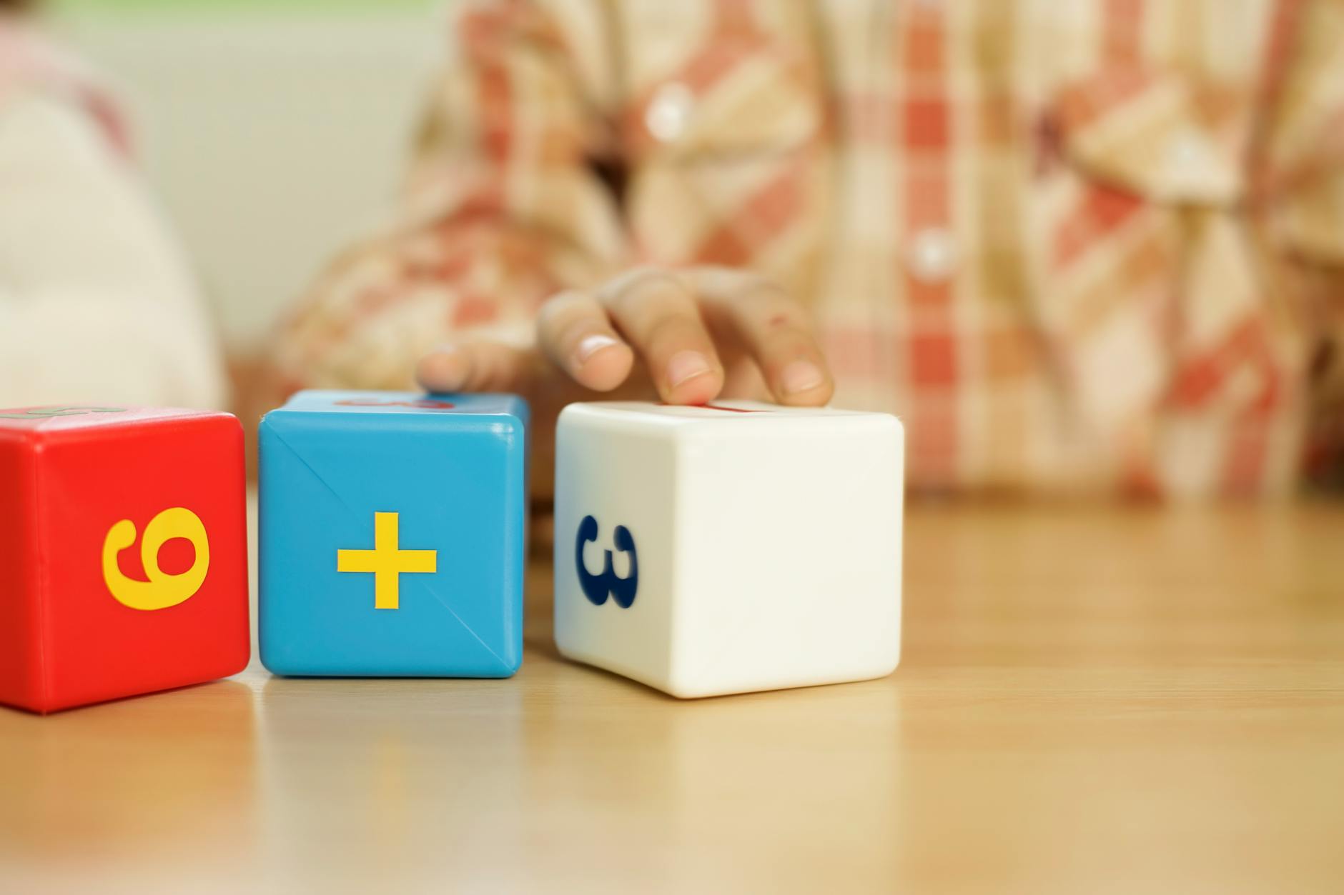 Dłoń dziecka dotyka kolorowych klocków z zadaniami matematycznymi Dłoń dziecka dotyka kolorowych klocków z zadaniami matematycznymi