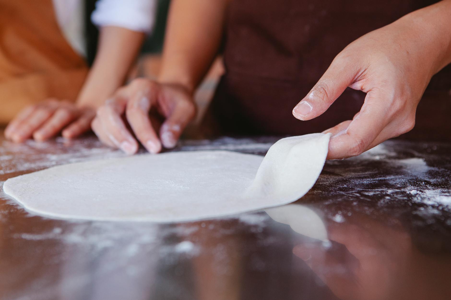 Dłonie formujące kulę ciasta do pizzy na oprószonym mąką blacie