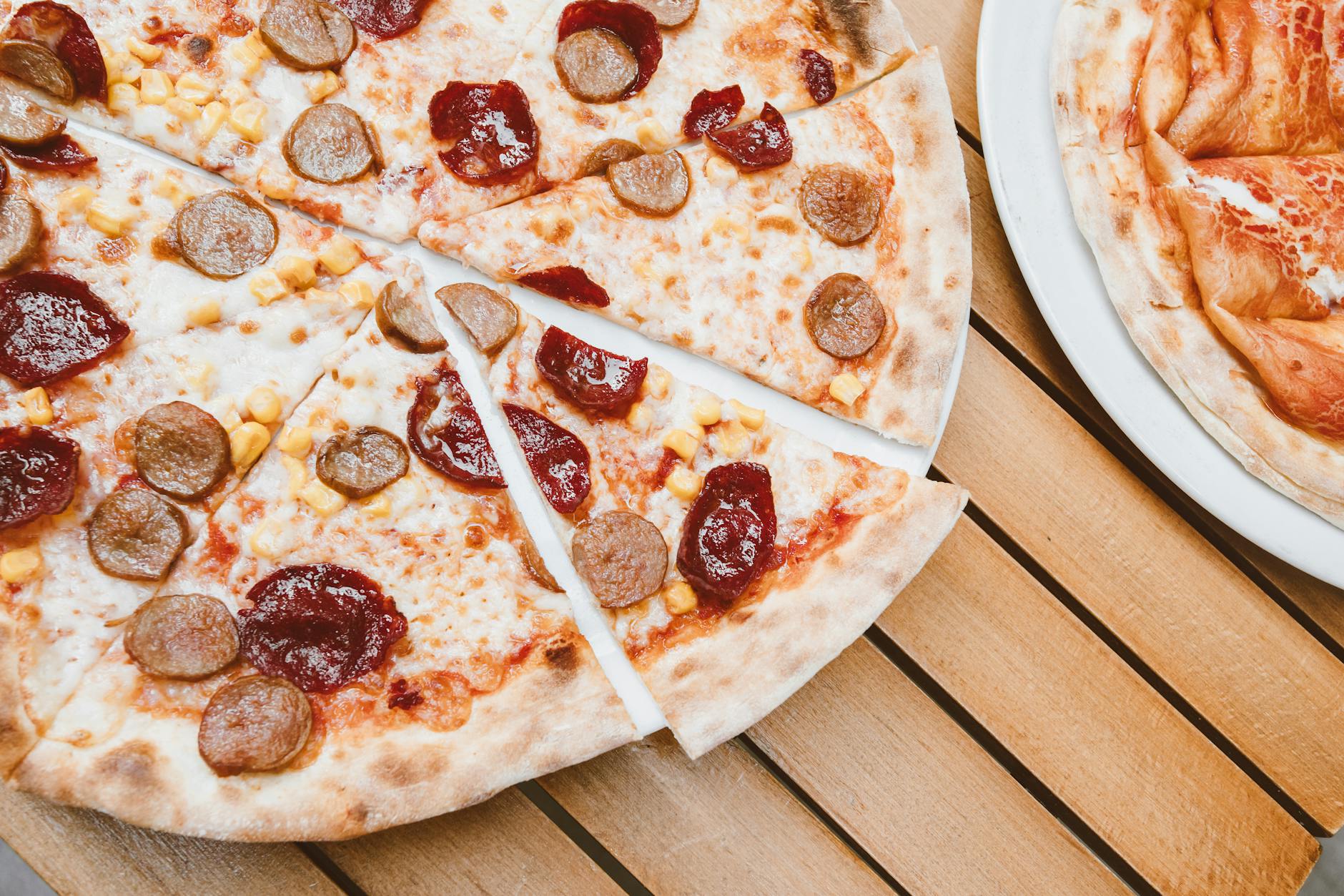Jak zrobić cienkie i chrupiące ciasto na pizzę bez doświadczenia w kuchni włoskiej Kawałki pizzy pepperoni z kiełbasą na rustykalnym drewnianym stole