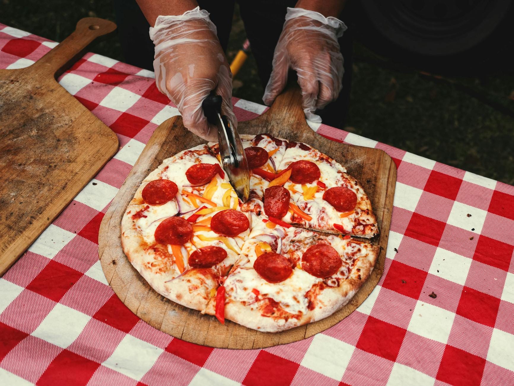 Kucharz kroi pepperoni pizzę na kraciastym obrusie na ulicznym straganie