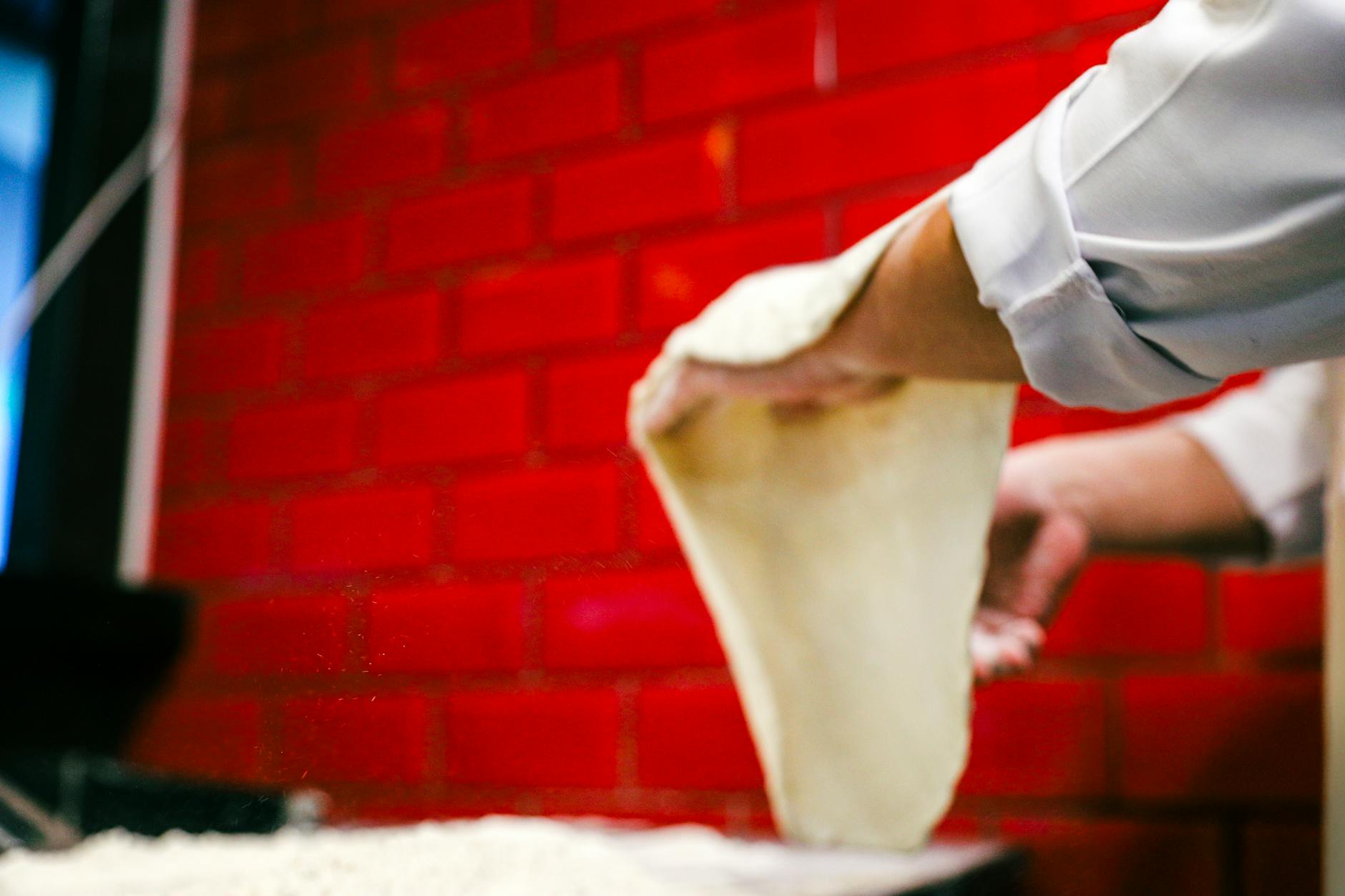 Sekrety dojrzewania ciasta do pizzy w chłodzie smak, struktura i planowanie pracy Kucharz rozciąga ciasto na pizzę w kuchni z czerwonej cegły