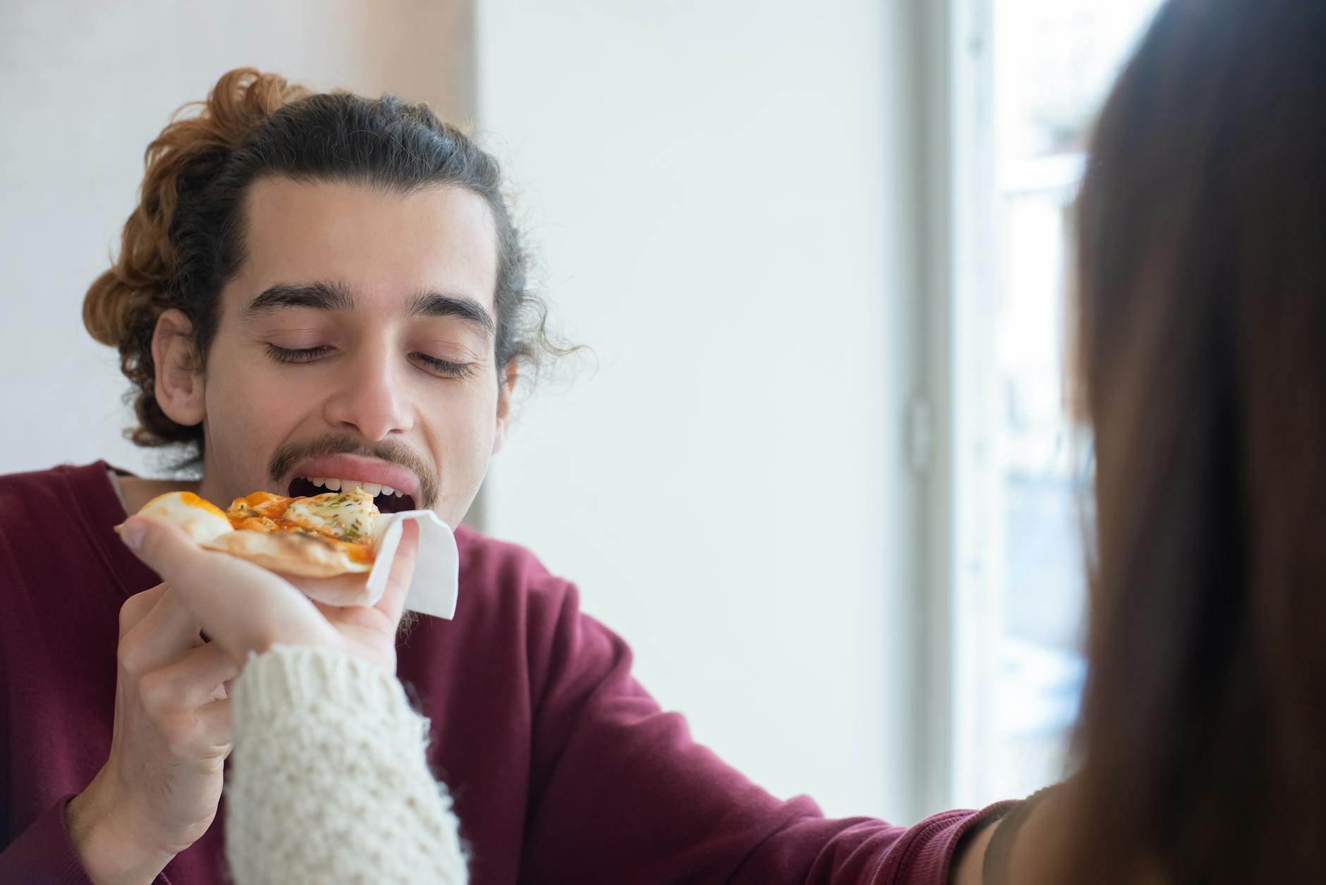 Mężczyzna bierze kęs pizzy podanej przez znajomego w przytulnym wnętrzu