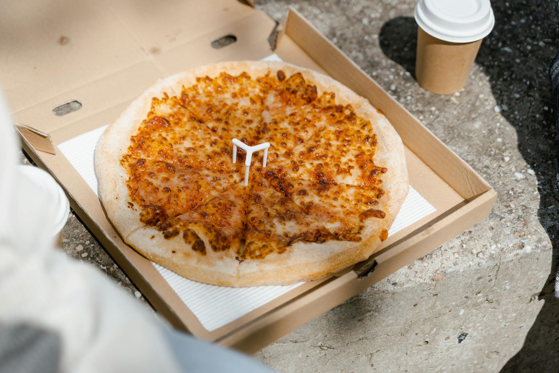 Pizza serowa w otwartym pudełku z jednorazowym kubkiem na dworze