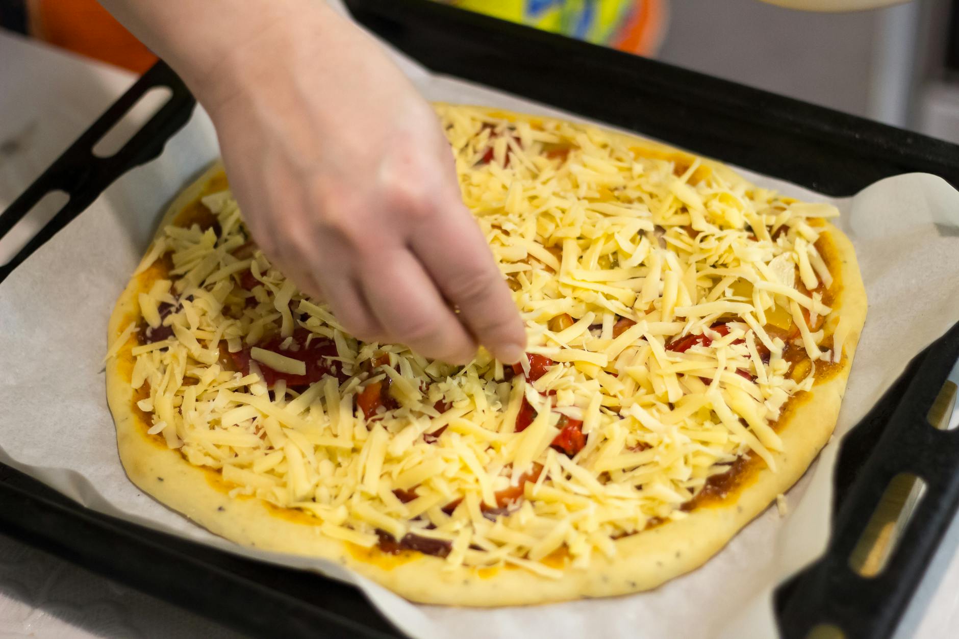 Dłoń posypująca starty ser na pizzy z licznymi dodatkami