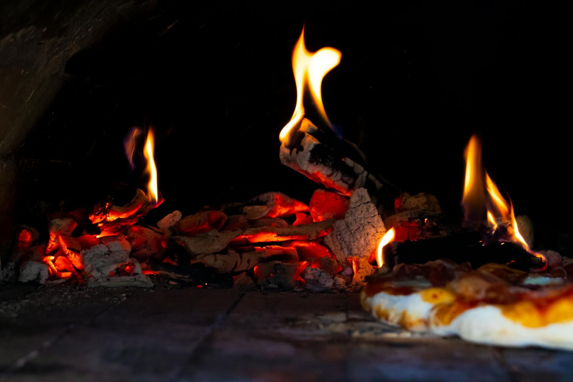 Pizza piecze się w kamiennym piecu opalanym drewnem z widocznym płomieniem Pizza piecze się w kamiennym piecu opalanym drewnem z widocznym płomieniem