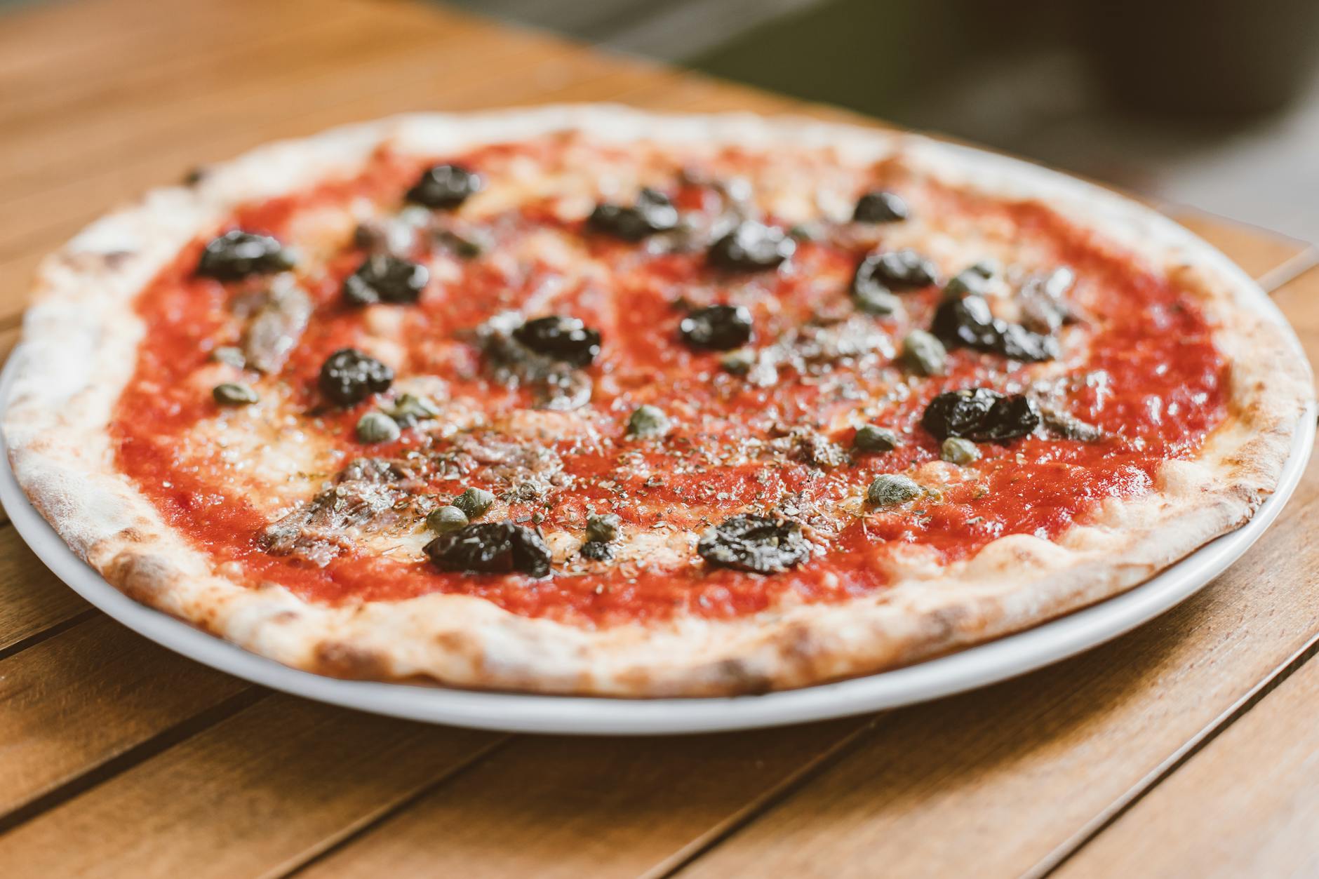 Pizza z sosem pomidorowym, czarnymi oliwkami i anchois na drewnianym stole