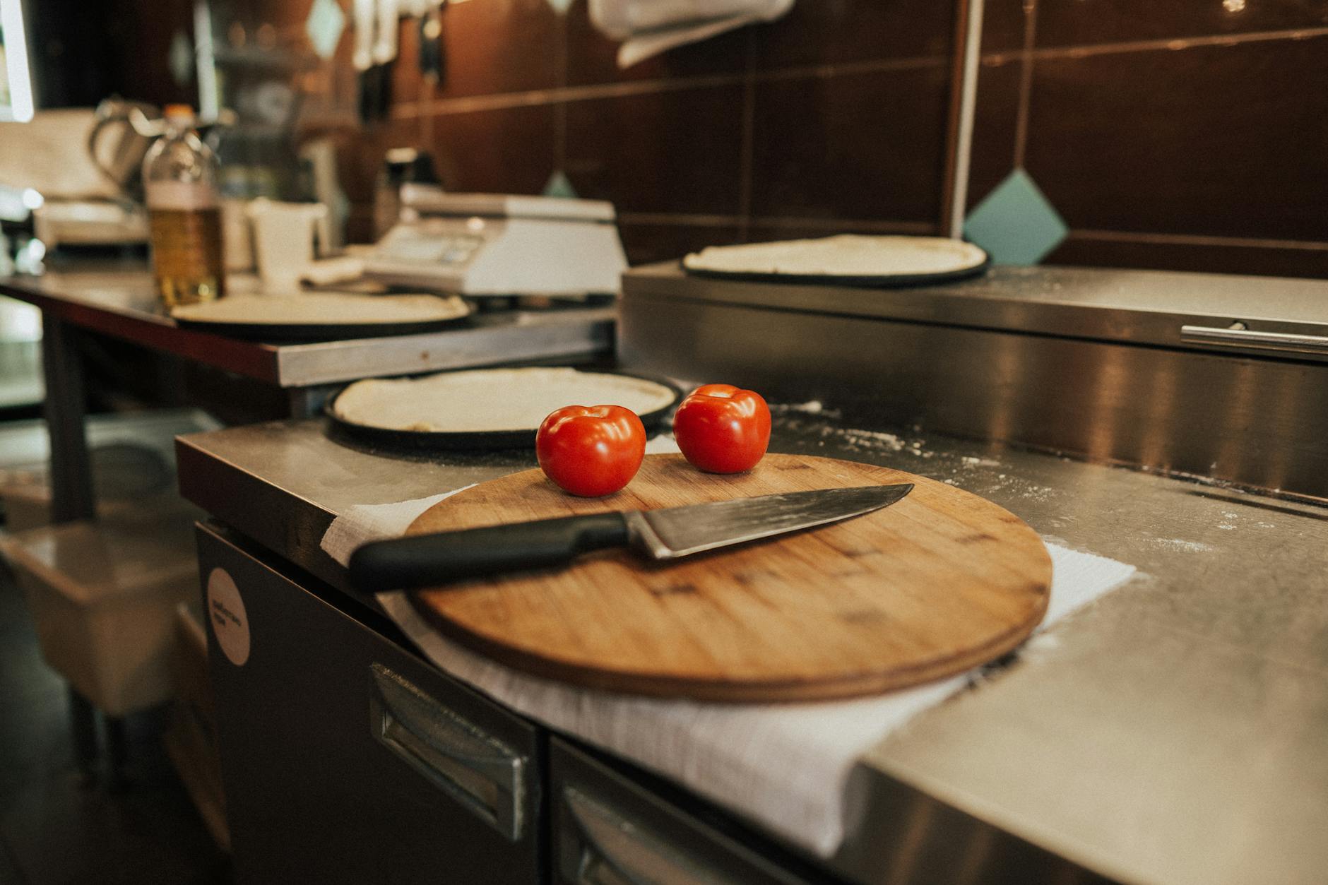 Pokrojone pomidory z nożem na desce obok ciasta na pizzę