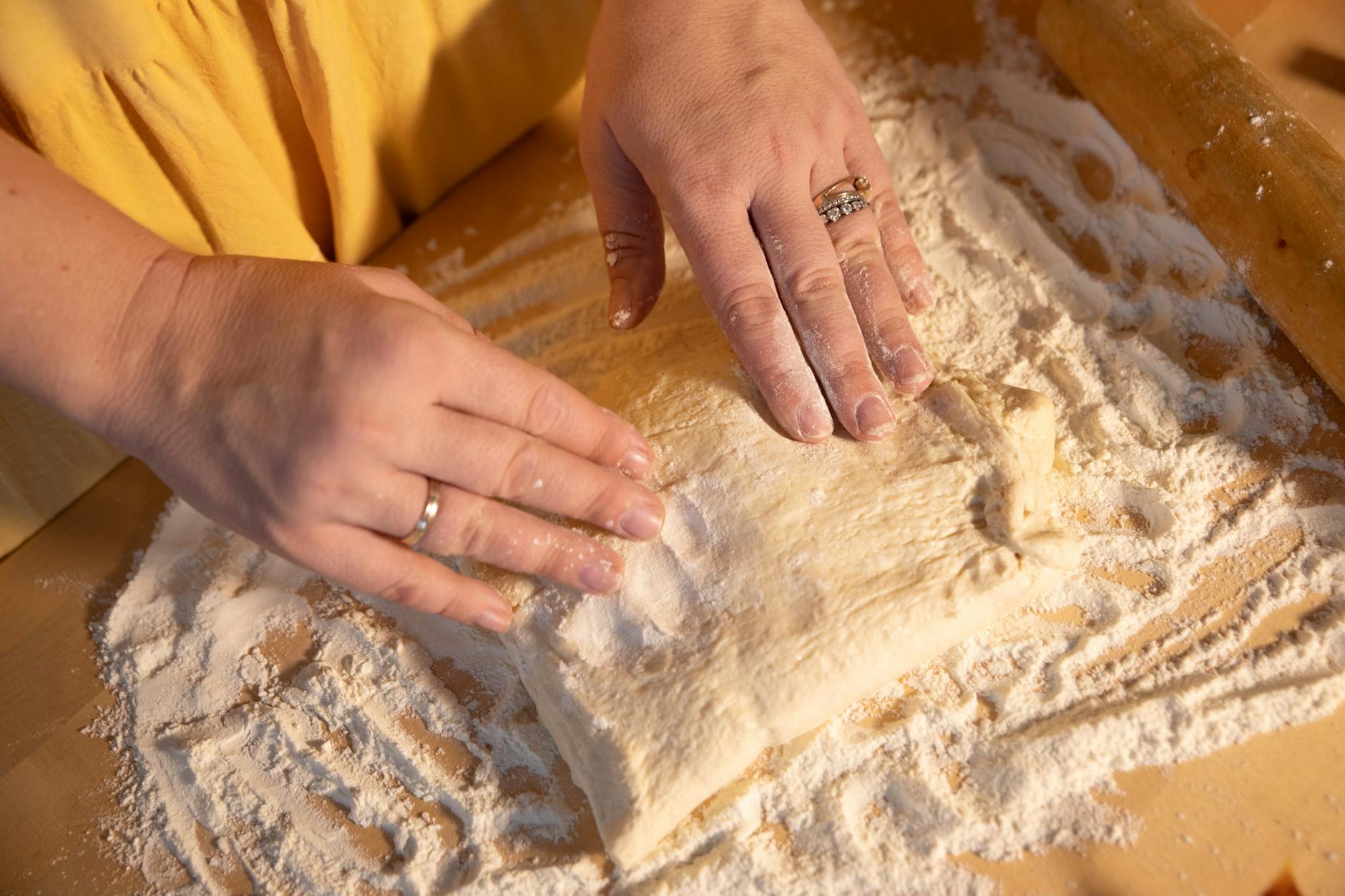 Ciasto do pizzy z długą fermentacją na chłodno pełen harmonogram pracy Ręce wyrabiające ciasto na pizzę na oprószonym mąką blacie drewnianym