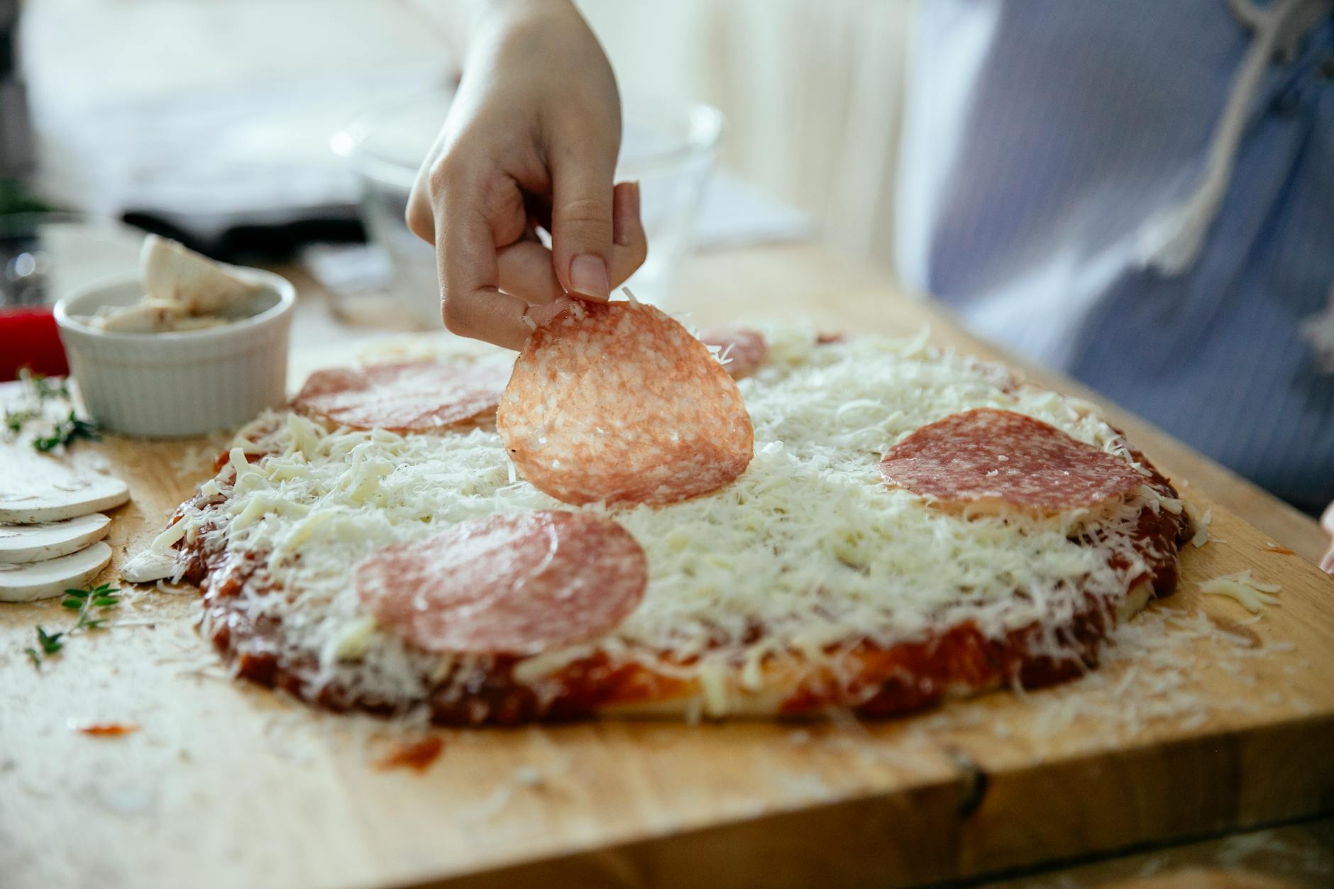 Układanie plasterków salami na domowej pizzy w kuchni