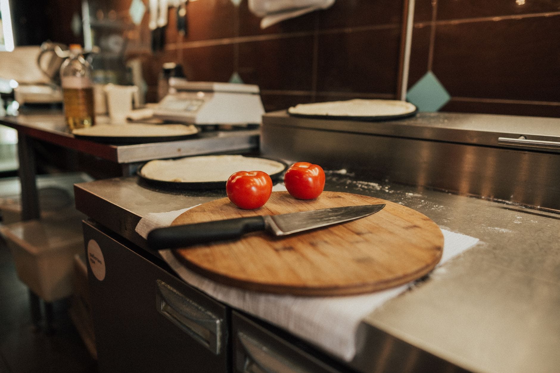 Jakie akcesoria do pizzy warto mieć pod ręką, by zawsze wychodziła idealnie chrupiąca Deska z pomidorami i nożem obok rozwałkowanego ciasta na pizzę