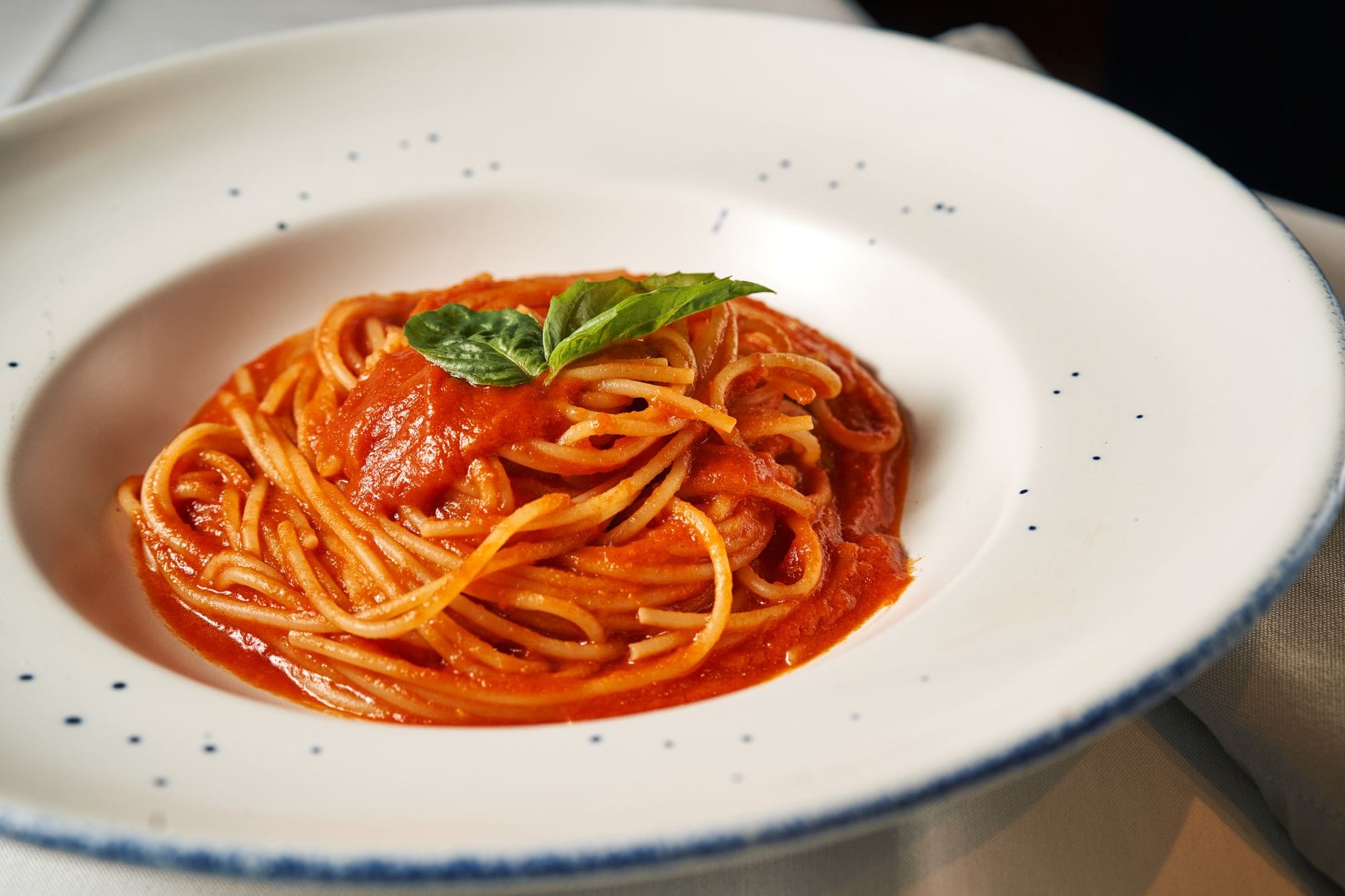 Spaghetti z sosem pomidorowym i listkami bazylii na talerzu
