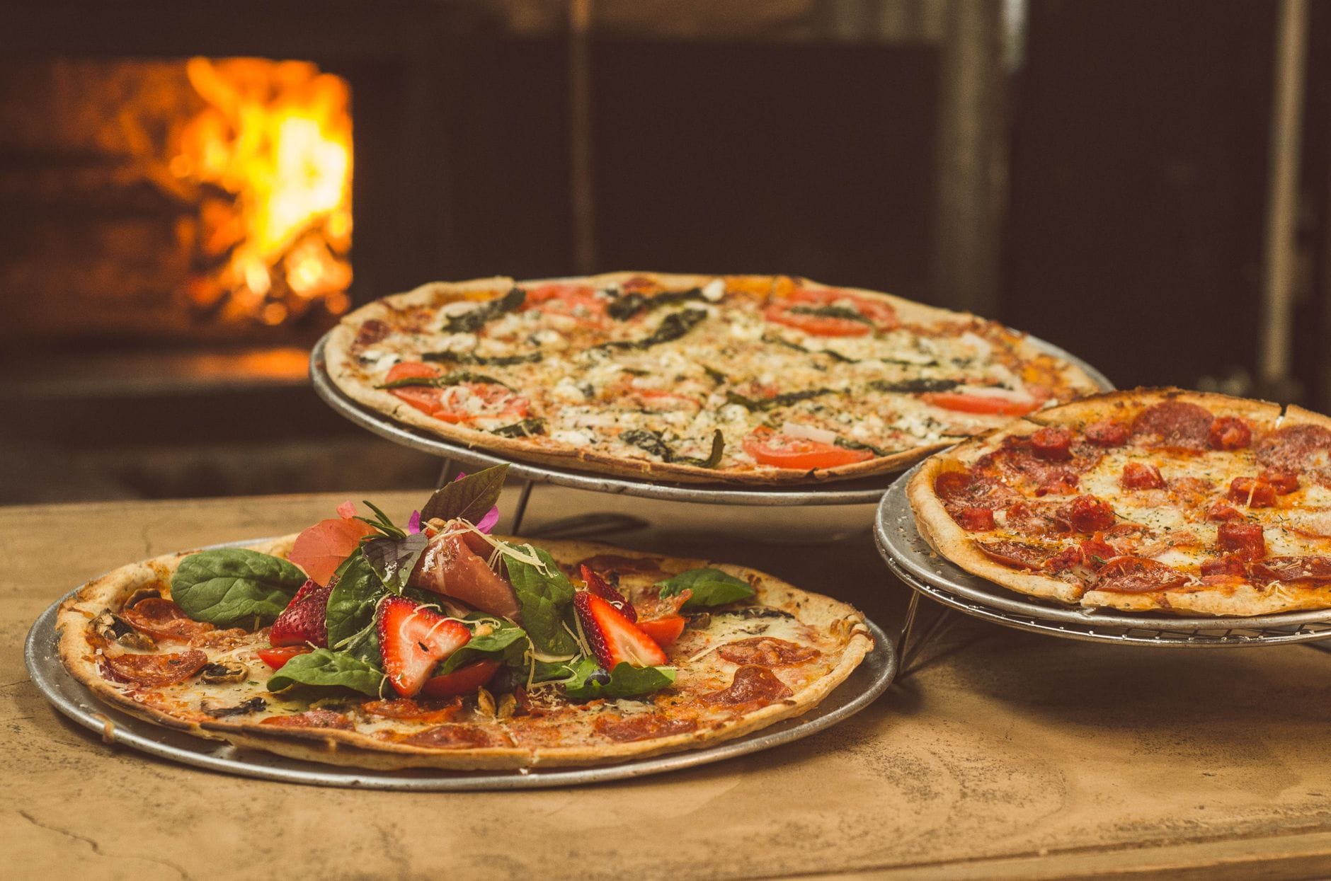 Trzy pizze gourmet przed piecem opalanym drewnem na tarasie